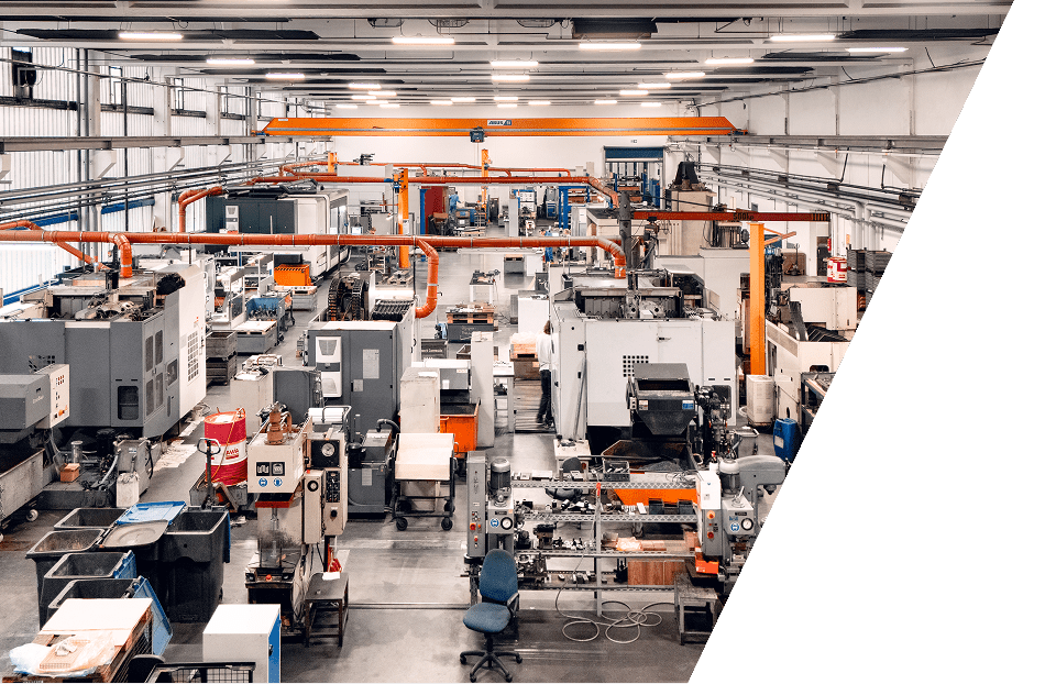 Ein großes, modernes Fabrikgebäude voller industrieller Maschinen, Arbeitsplätze und Geräte. An der Decke sind orangefarbene Kräne angebracht, und in dem sauberen, organisierten Raum sind verschiedene Werkzeuge und Wagen verteilt.